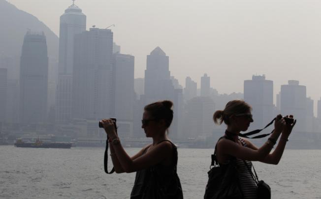 Two tourists focus their cameras to the backdrop of thick smog that has become all too familiar on Victoria Harbour. Photo: Felix Wong