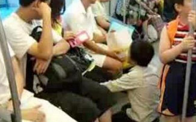 A panhandler kneels in front of the commuters on a Shanghai subway train. Photo: SCMP