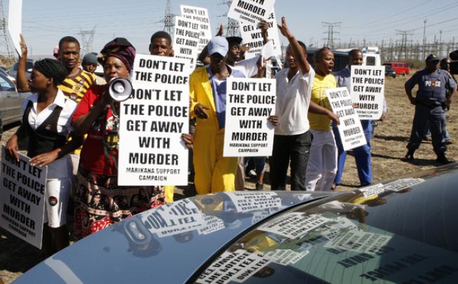 Protestors holding placards greet the judicial panel investigating the shootings at Lonmin's platinum mine in Marikana on Monday. Photo: AP 