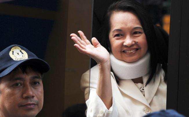 Former Philippine president Gloria Arroyo waves to photographers from a vehicle after appearing in court for her arraignment in February. Photo: AFP
