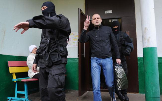 Ultra-left opposition leader Sergei Udaltsov flashes the V-sign for victory as he follows masked Interior Ministry officers taking him in for questioning after the search of his home in Moscow on Wednesday. Photo: AFP