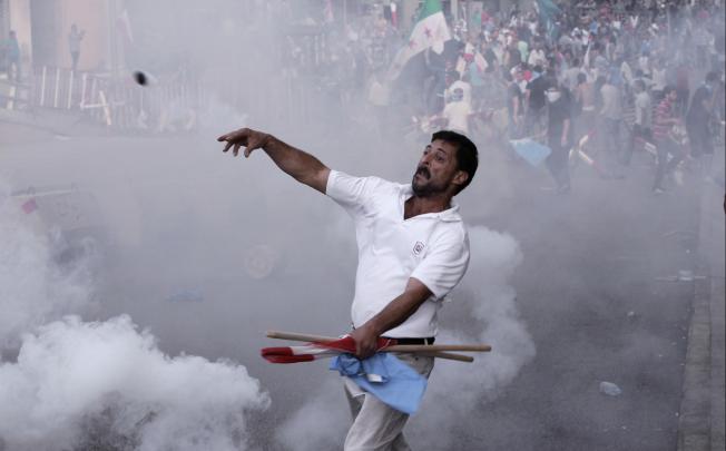 A protester throws a tear gas canister back at security forces during clashes after Wissam al-Hassan's funeral. Photo: AP