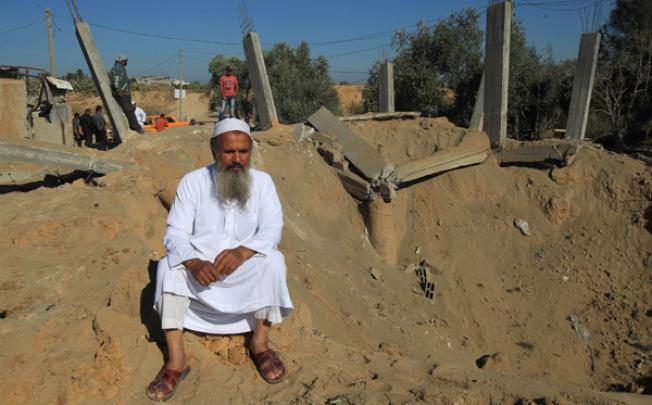 A Palestinian man sits on th edge of a crater following an Israeli attack that damaged a building in al-Bureij, in the centre of the Gaza Strip, on Monday. Photo: AFP 