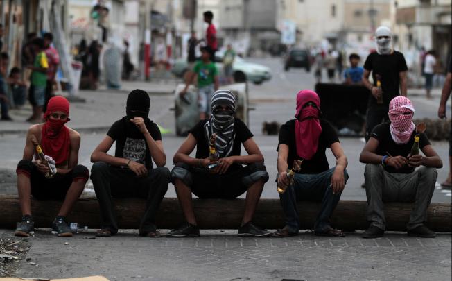 Masked Bahraini anti-government protesters holding petrol bombs sit on a telephone pole being used as a roadblock ahead of a march in Malkiya, Bahrain on Sunday, October 28. Photo: AP