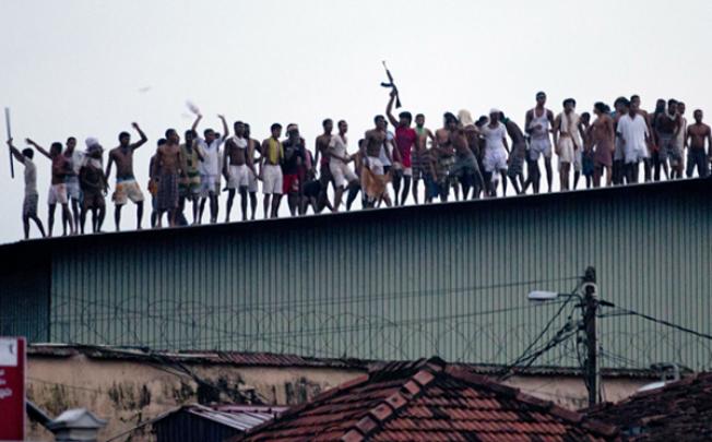 Sri Lankan inmates display guns, throw stones and shout slogans from the roof of Welikada prison in Colombo on Friday. Photo: AP