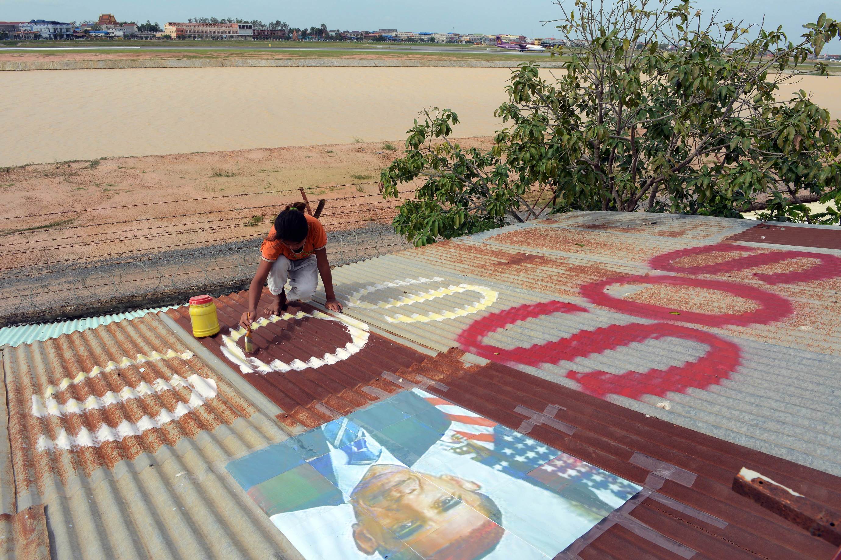 A Cambodian girl paints the word SOS under a portrait of US President Barack Obama on a roof next to Phnom Penh airport on Thursday. Photo: AFP 