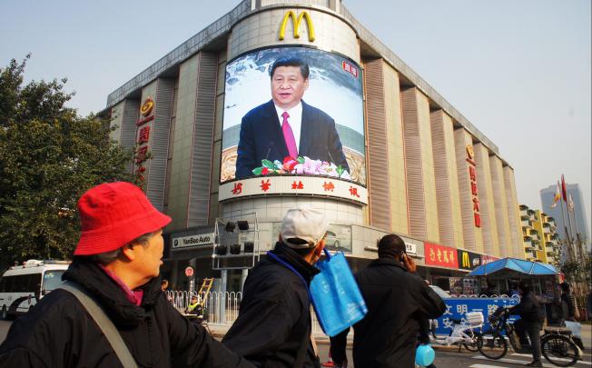 People walk across a street as a screen shows Xi Jinping, head of the Communist Party, in Beijing on November 15, 2012. Photo: EPA