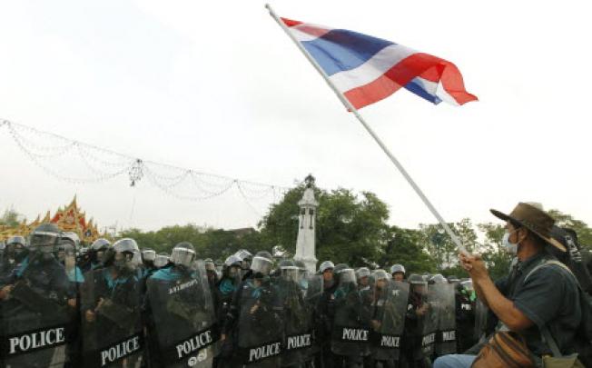 A anti-government Pitak Siam wave Thai national flag in front of Thai riot polices at Makkawan bridge near the Government House in Bangkok on Thailand. Photo: EPA