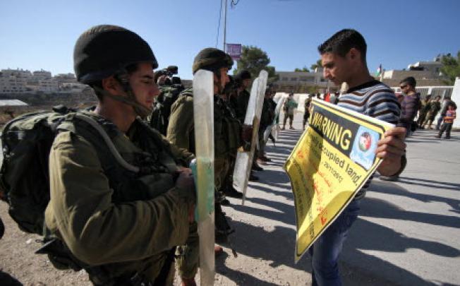 A Palestinian protester holds a banner reading "WARNING: This is illegally occupied land. State of Palestine." as Israeli soldiers stand guard during a demonstration against Israel's controversial separation barrier in the West Bank village of Al-Maasarah near Bethlehem on Nov. 30, 2012. Photo:Xinhua