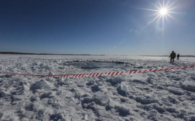 Russian policeman stands near an 8m hole, reportedly the site of a meteorite fall, in the ice of the frozen Chebarkul lake about 8km from Chelyabinsk, Urals, Russia. Photo: EPA
