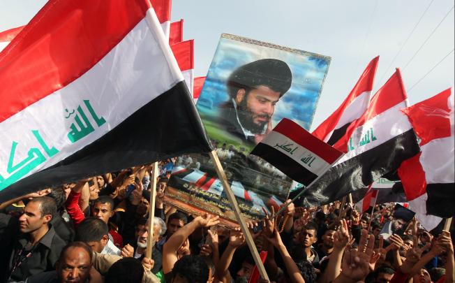 Iraqi followers of Shiite Muslim cleric Moqtada al-Sadr (portrait) wave national flags during a protest on Saturday in the city of Kut, south of the capital Baghdad, on the tenth anniversary since the US-led invasion of Iraq. Photo: AFP
