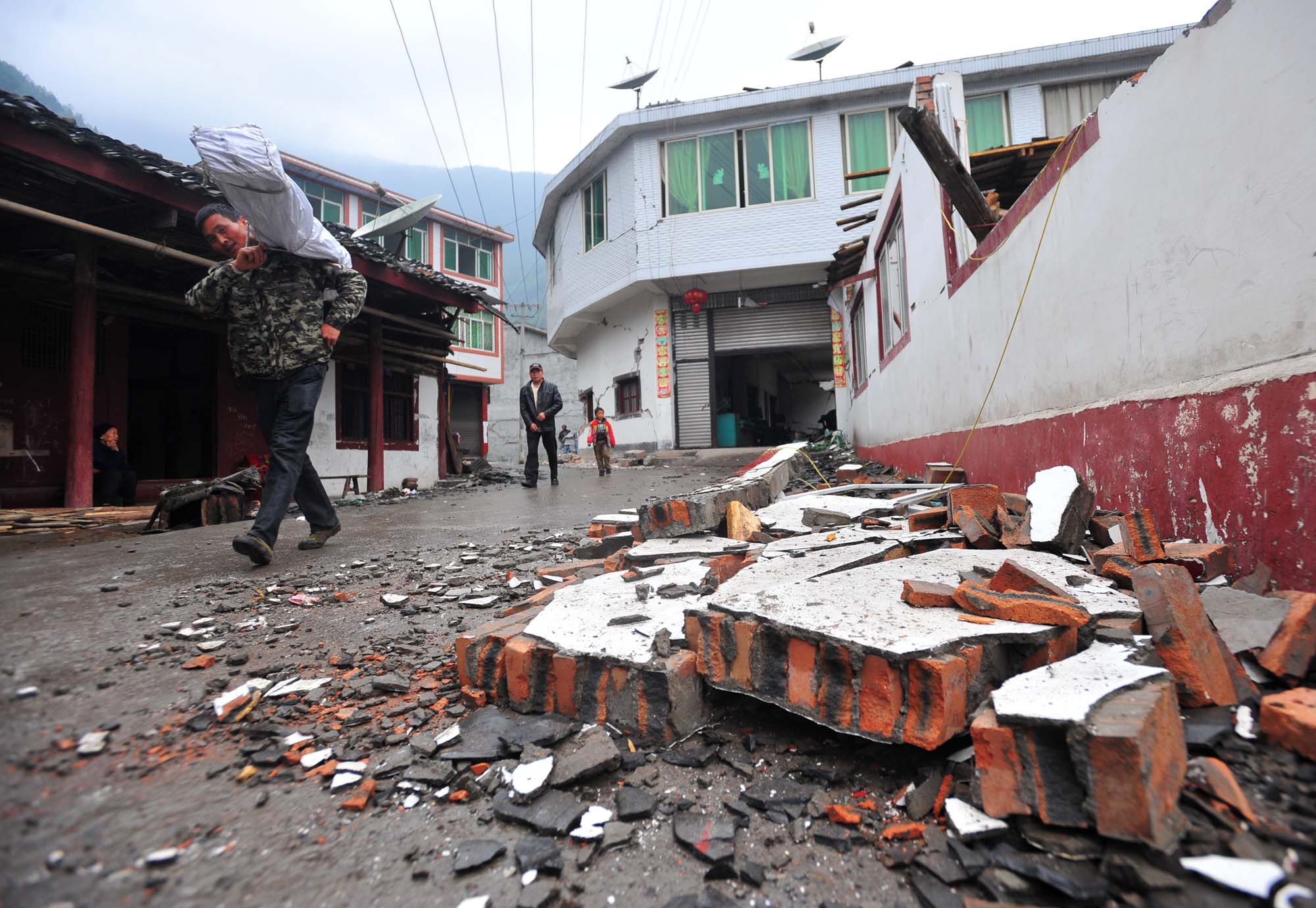 Villagers walk past a damaged house in quake-hit Yuxi Village of Lushan County. Photo: Xinhua