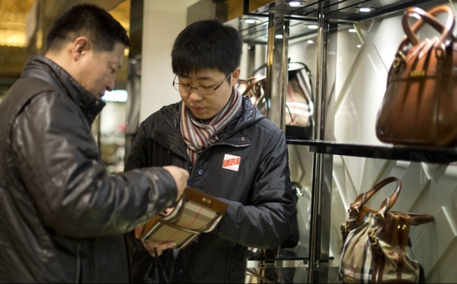 A Chinese couple visiting the exclusive Harrods department store in London consider splashing out on an expensive handbag. Photo: AFP