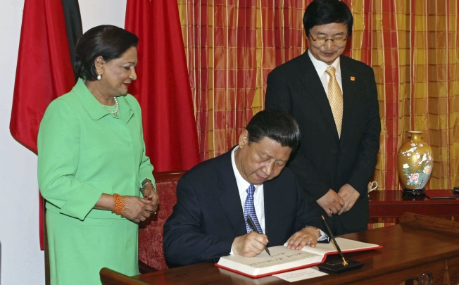 Chinese President Xi Jinping, center, signs the guest book watched by Trinidad and Tobago's Prime Minister Kamla Persad-Bissessar, left, at the Diplomatic Center in St. Ann's, Trinidad. Photo: AP