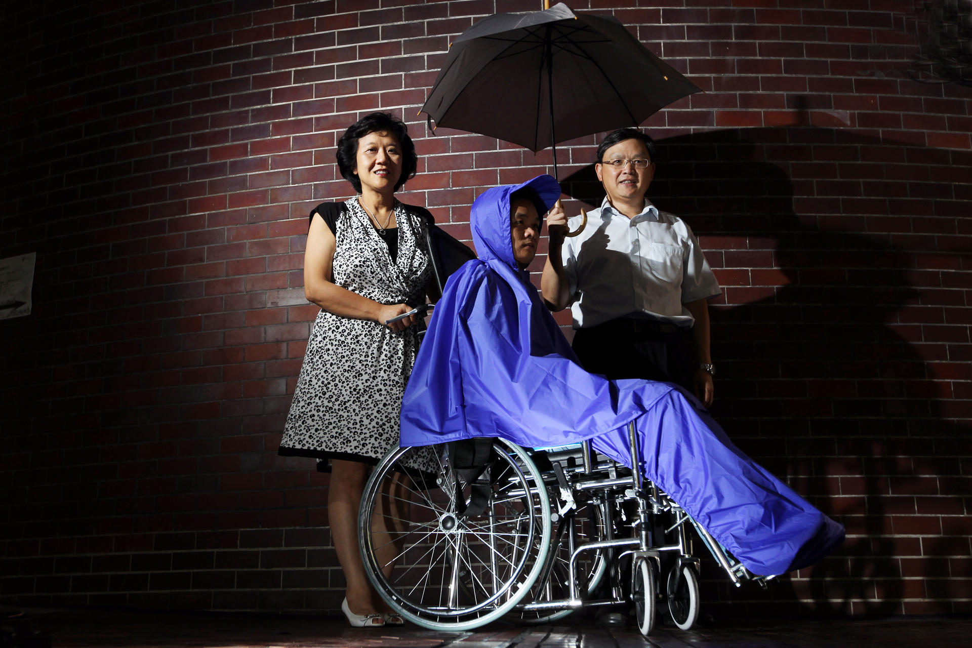 Frency Ng (left) and Patrick Hui (right) with a man wearing a raincoat designed for people in wheelchairs. Photos: Nora Tam