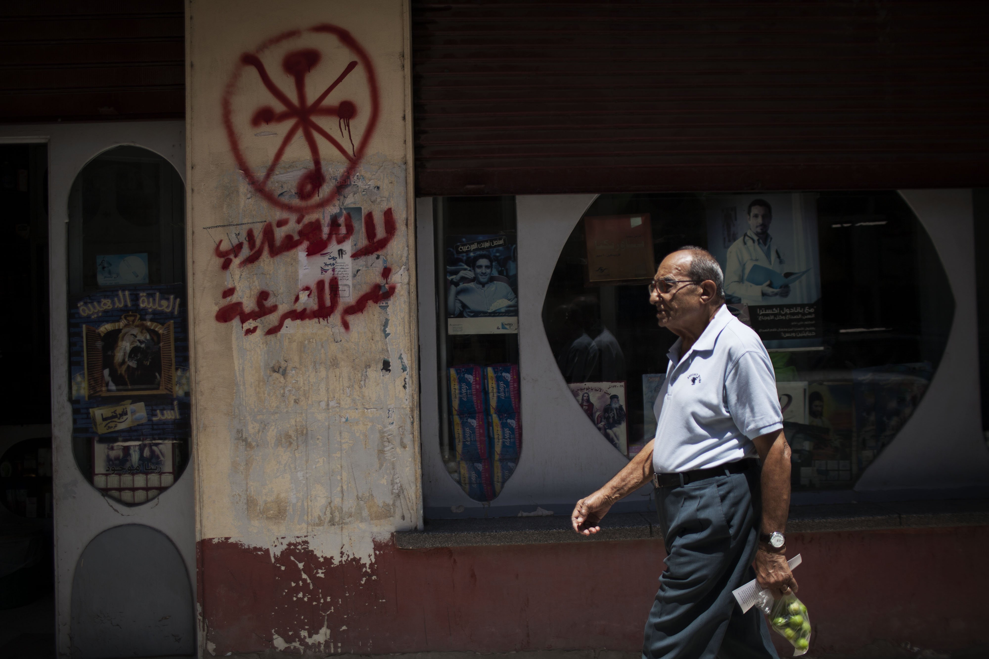 An Egyptian man walks in front of a pharmacy marked with anti-Coptic and anti-coup graffiti. Photo: AP