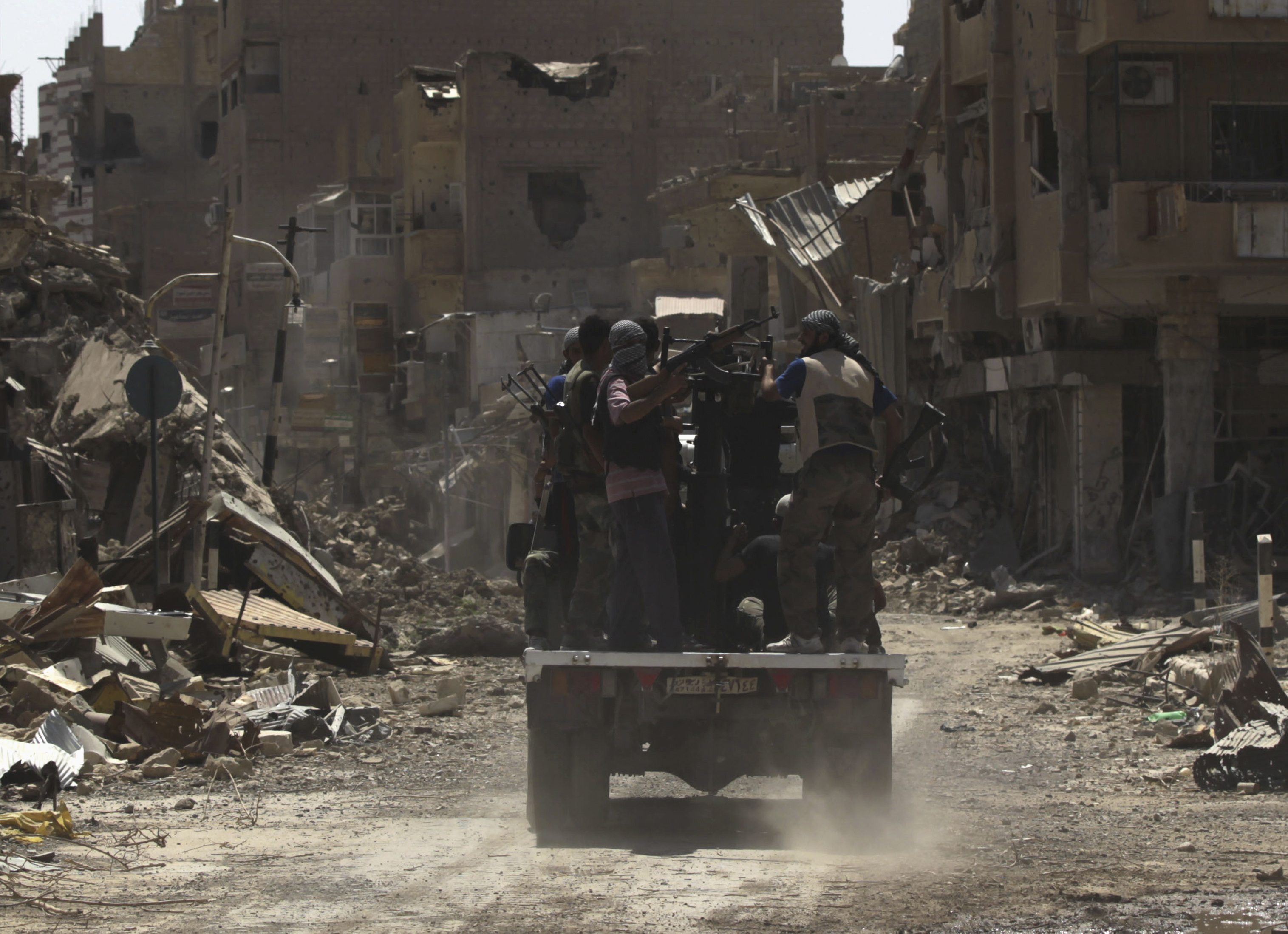 Free Syrian Army fighters carry their weapons as they ride on a pick-up truck mounted with an anti-aircraft weapon at a damaged street in Deir al-Zor. Photo: Reuters