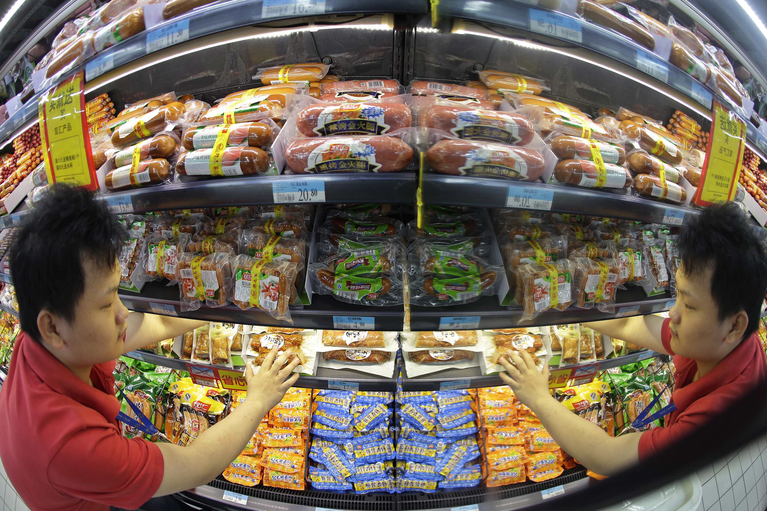 A shop worker is reflected in a mirror as he arranges display of meat products of Shuanghui (Shineway) Group at a Wuhan supermarket. Photo: Reuters