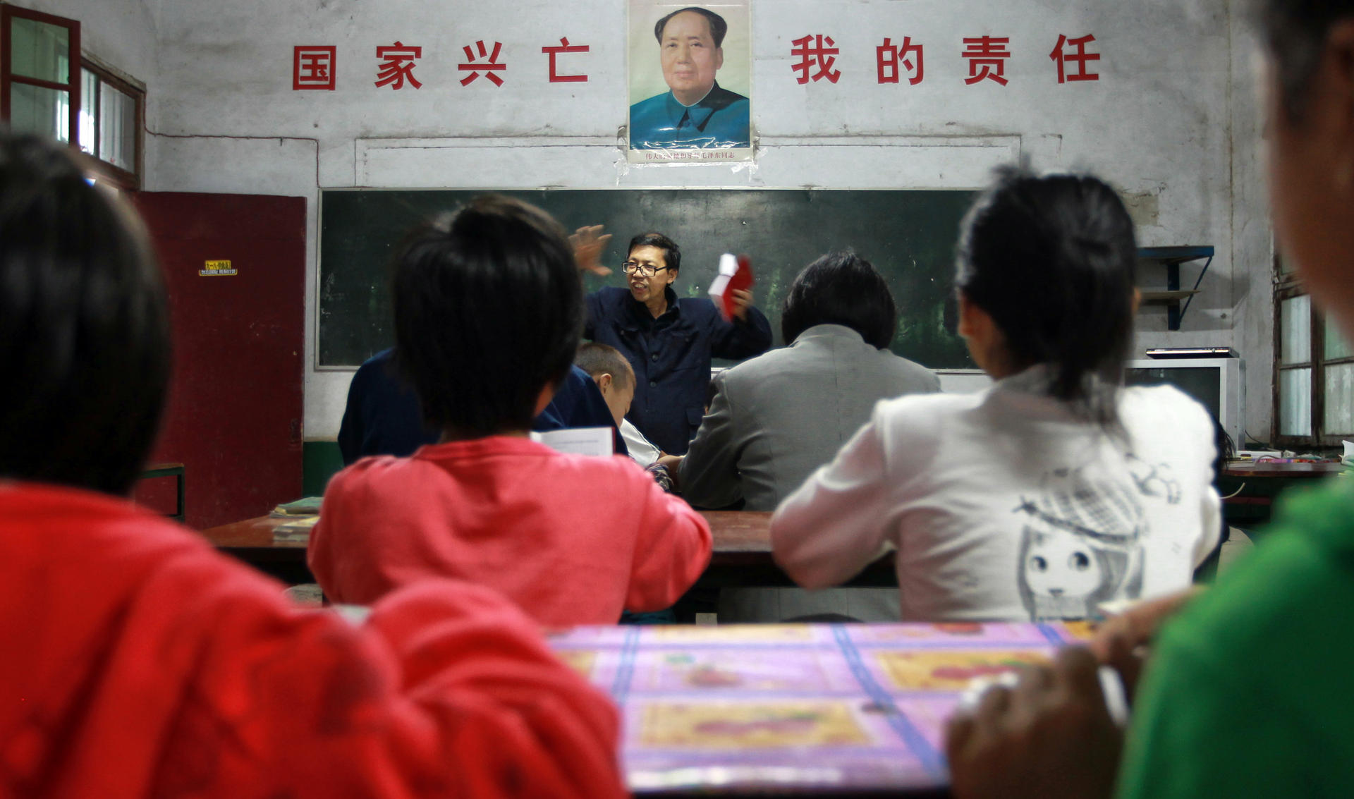 Democracy School principal Xia Zuhai holds a copy of Mao Zedong's little red book as he delivers a speech during morning class on September 9, the 37th anniversary of Mao's death. The slogan on the wall says: "The country's rise and fall is my responsibility."