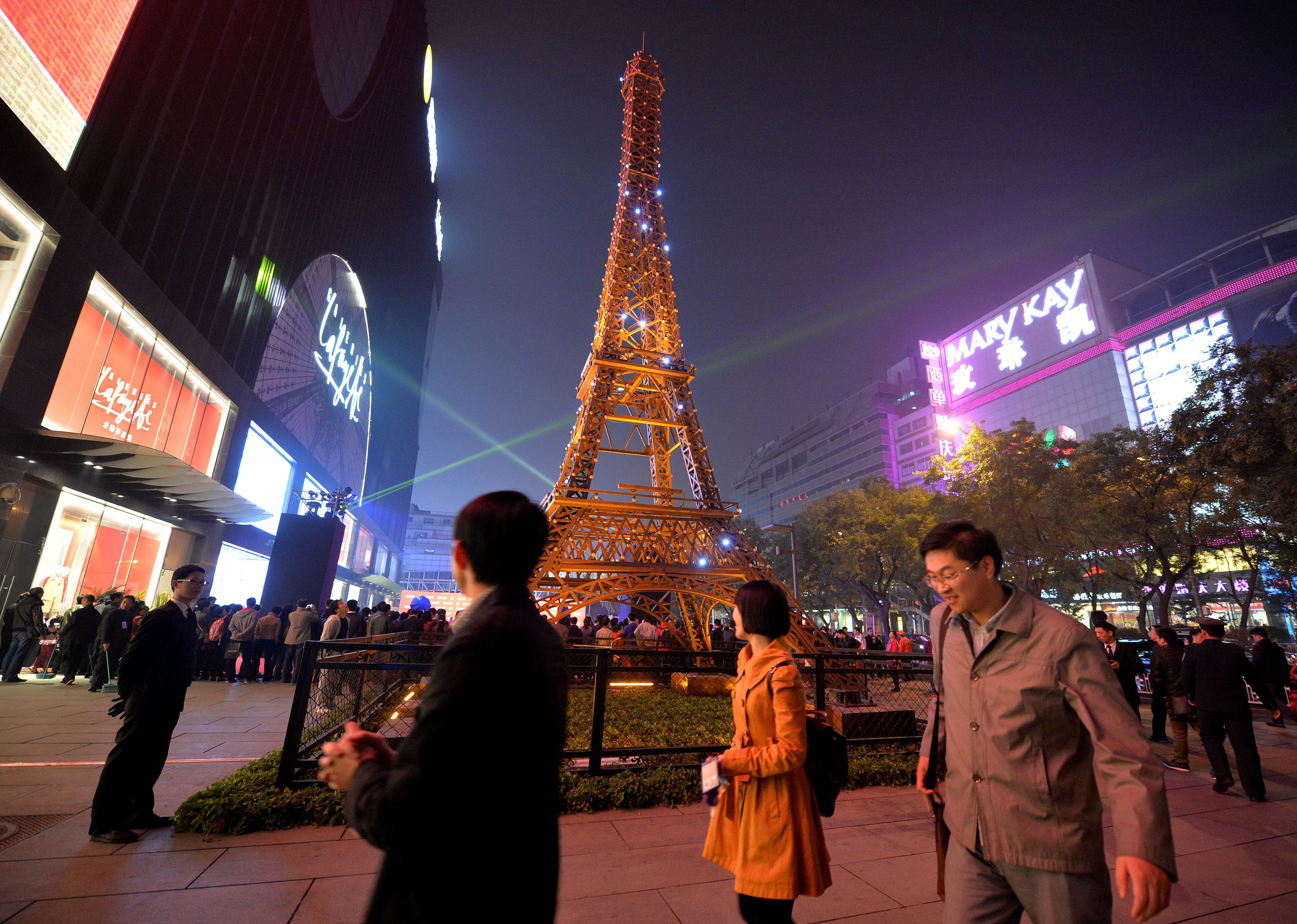 Chinese shoppers stand beside a model of the Eiffel Tower outside the Galeries Lafayette department store during its official opening in Beijing in October, 2013. Photo: AFP