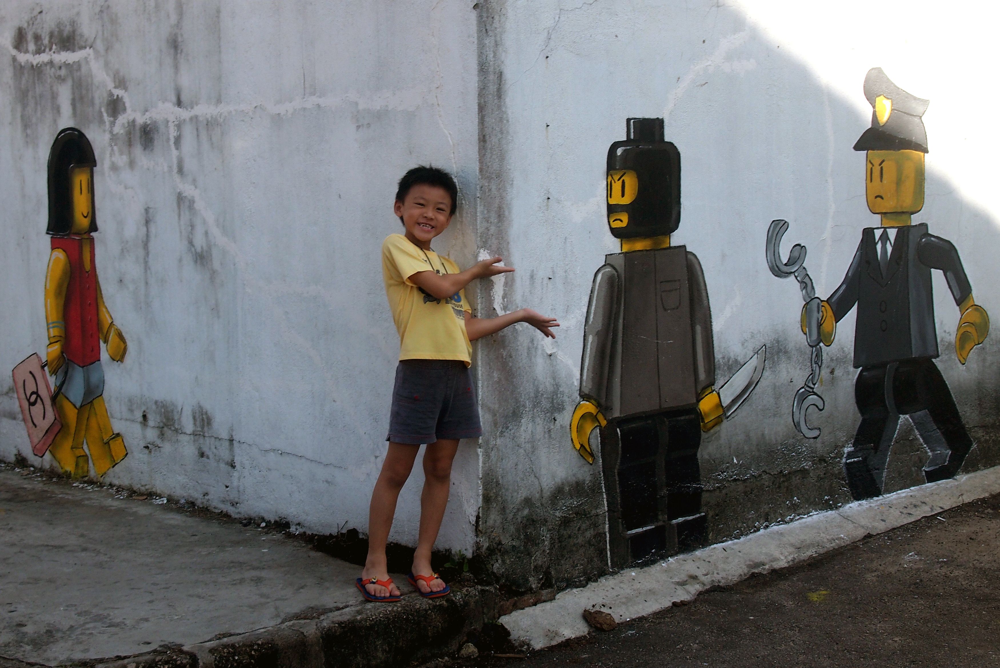 A boy next to a mural by Lithuanian artist Ernest Zacharevic, which shows a Lego woman with a Chanel bag, a Lego robber armed with a knife and a Malaysian policeman in Johor Bahru. Photo: AFP