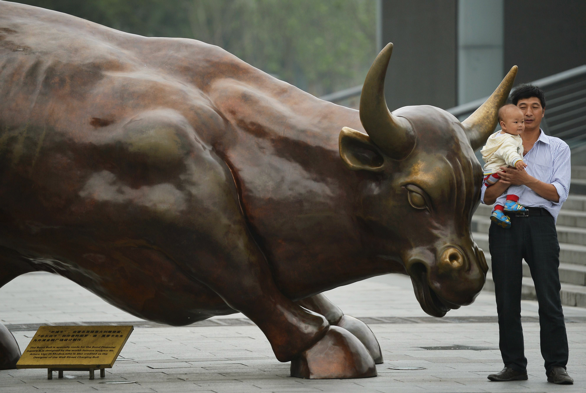 A father carries his baby next to the replica of the famous Wall Street bronze bull on the Bund in Shanghai. Photo: AFP