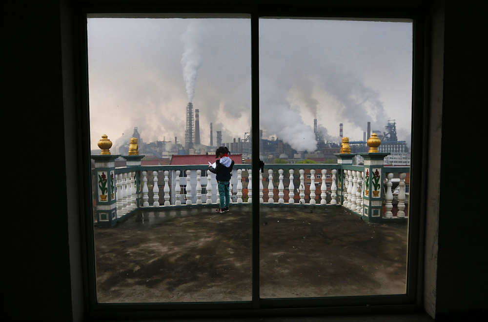 A girl reads a book on her balcony as smoke rises from chimneys of a steel plant in Quzhou, Zhejiang. Photo: Reuters