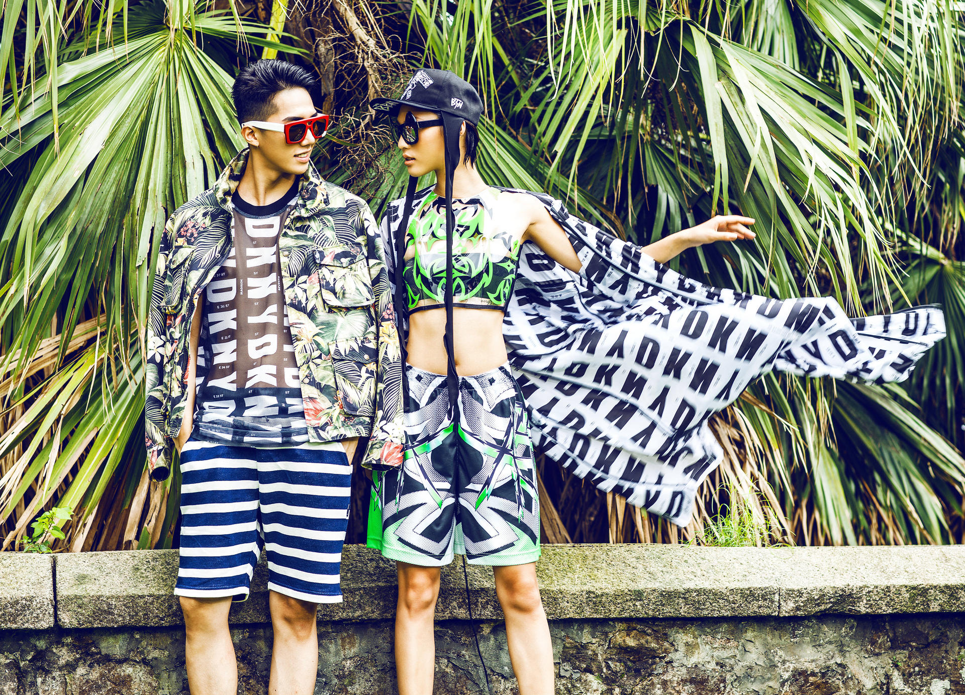 Yang Hoon wears a flower print jacket (HK$5,799) by Ami at I.T; logo scoop-neck tank top (HK$2,290) by DKNY; striped shorts (HK$399) by Izzue; red sunglasses (HK$2,750) by Numero at Lane Crawford. 
Xin Jie wears an HQ logo print anorak (HK$12,000) from DKNY; plastic crop top (HK$2,360); ninja print shorts (HK$1,630) by ASSK at Off the Wall; black skull embroidery double snapback (HK$2,360) by Kye at Off the Wall; black sunglasses (HK$2,900) by Revé by René at Woaw.