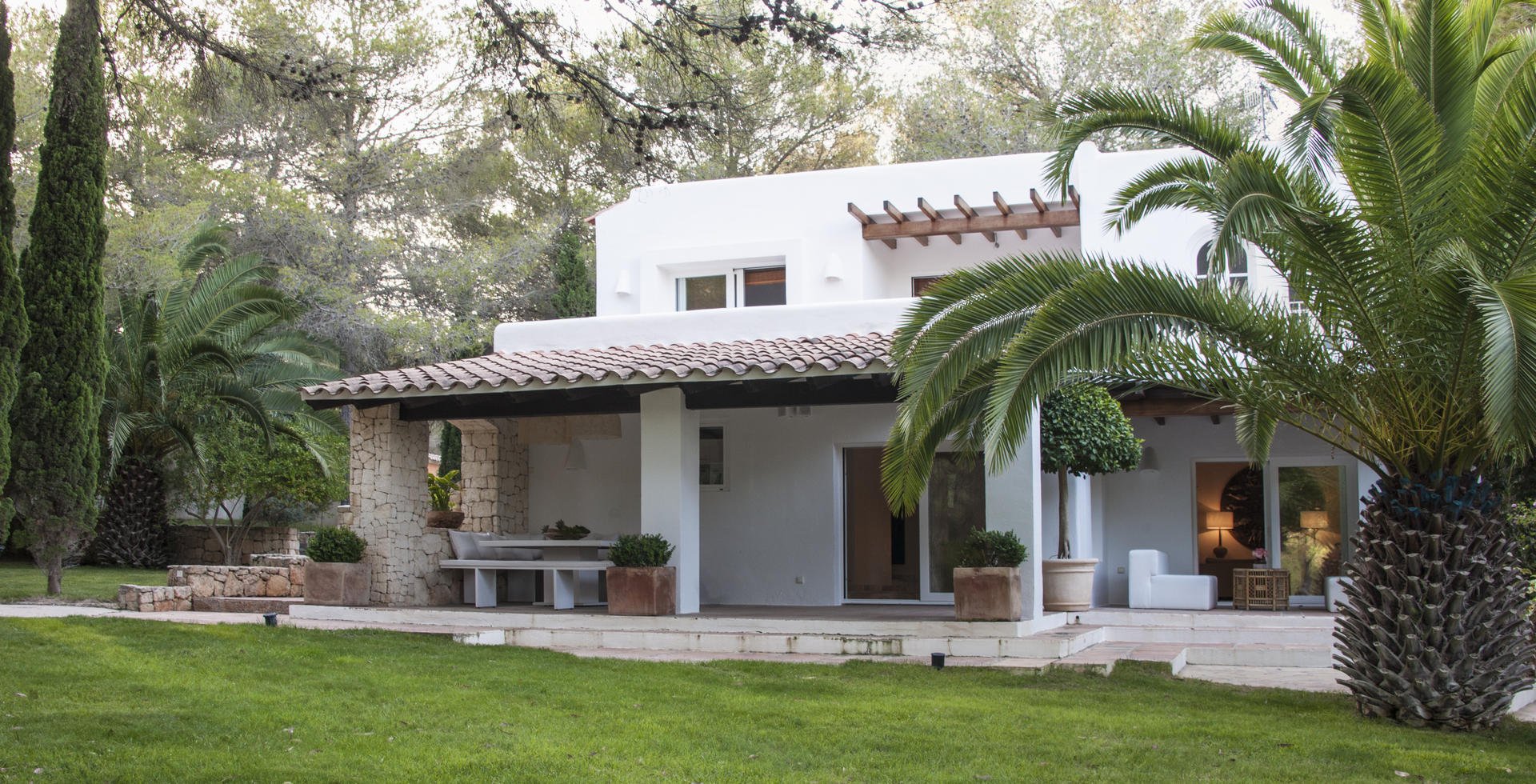 The exterior of the main house with large pine trees and ancient Phoenix palms.
