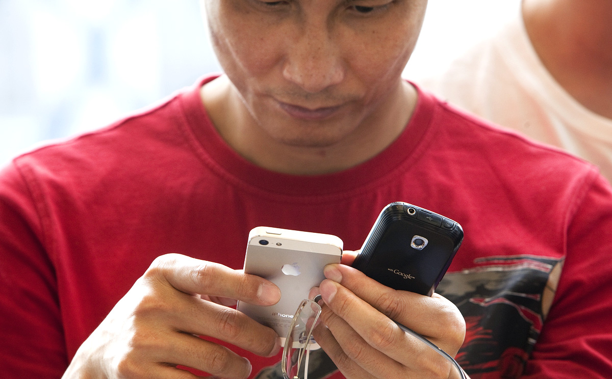 A man examines an iPhone 5 while holding an Android smartphone in his other hand. Photo: Bloomberg