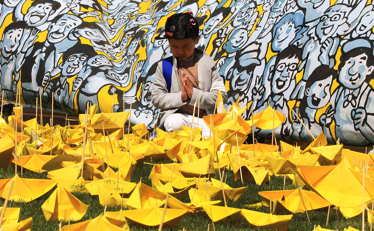 A boy prays near paper ships with messages to the victims of the sunken ferry Sewol at a memorial altar in Seoul. Photo: AP