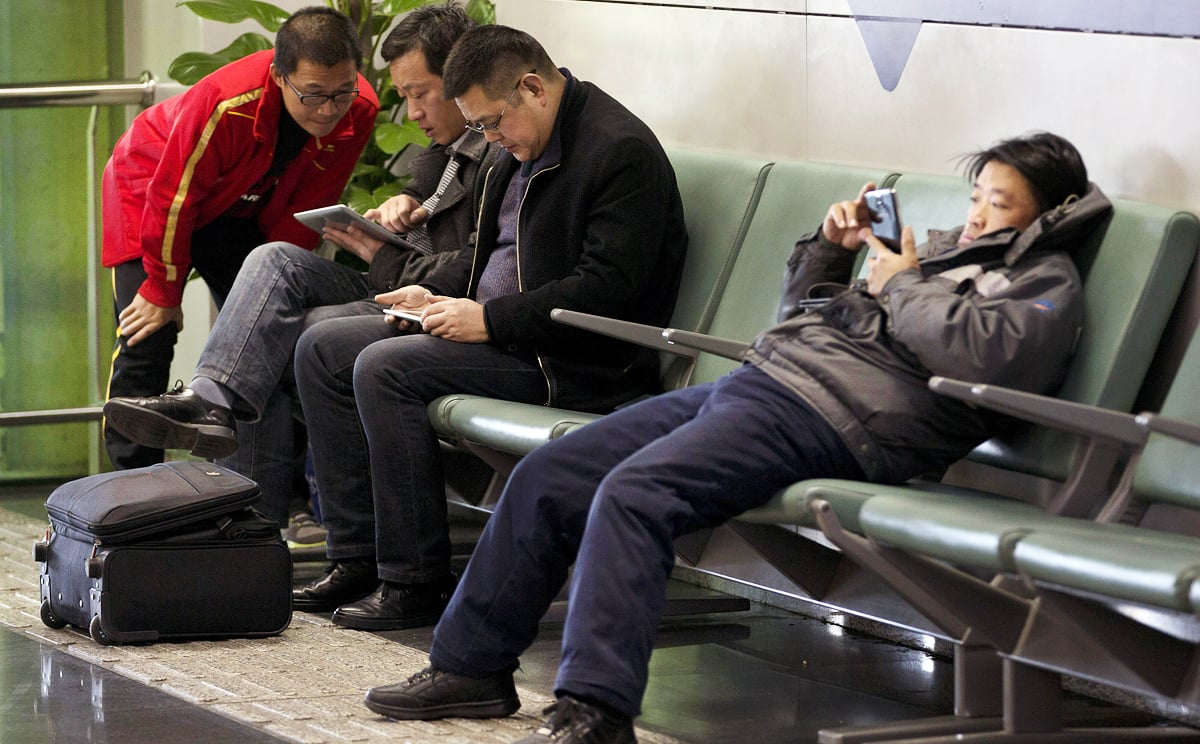 Men browse their tablet computers and smartphone at the Beijing Capital Airport in Beijing. Photo: AP