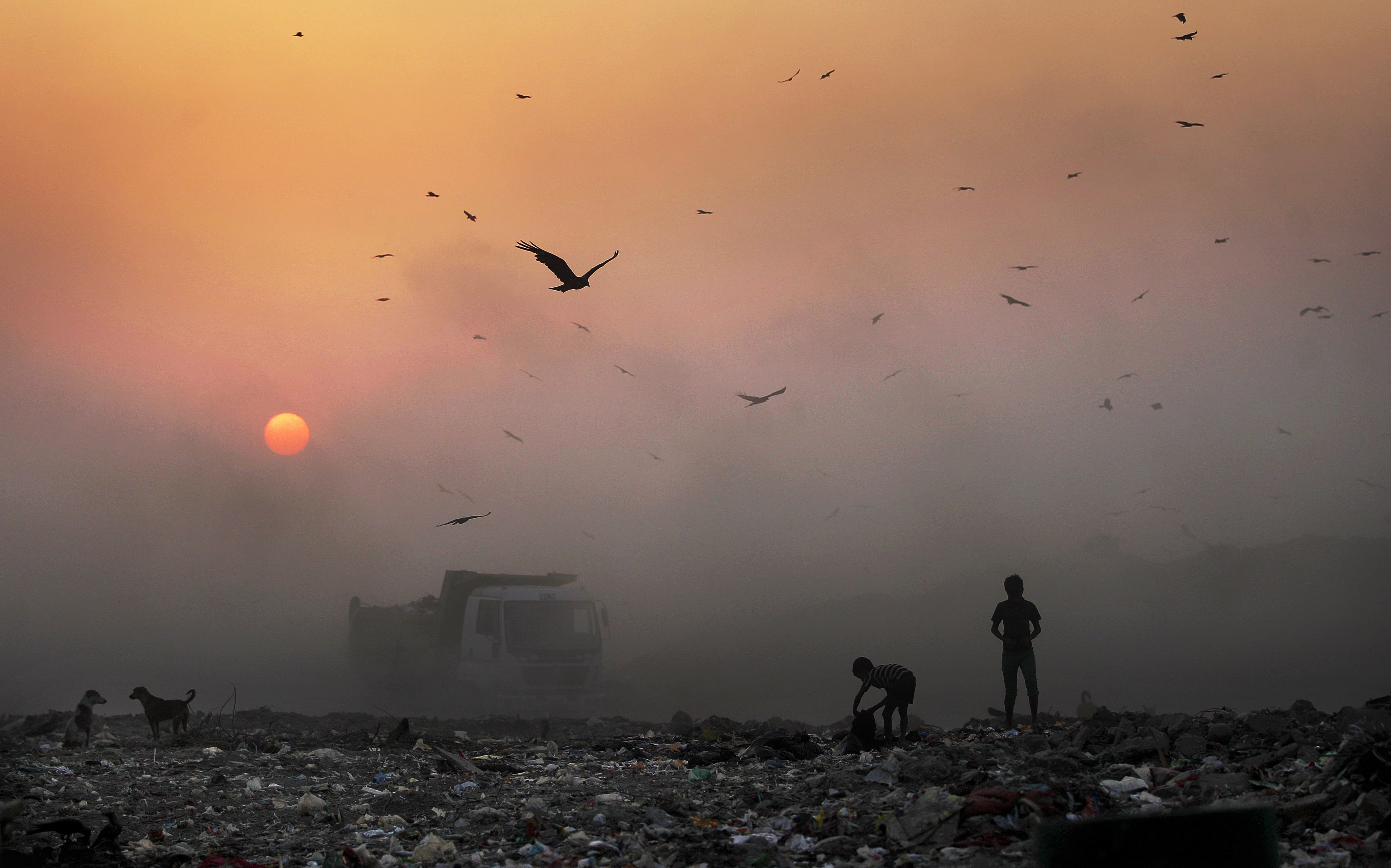 A thick blanket of smoke is seen against the setting sun as young ragpickers search for reusable material at a garbage dump in New Delhi, India on October 17, 2014. Photo: AP 