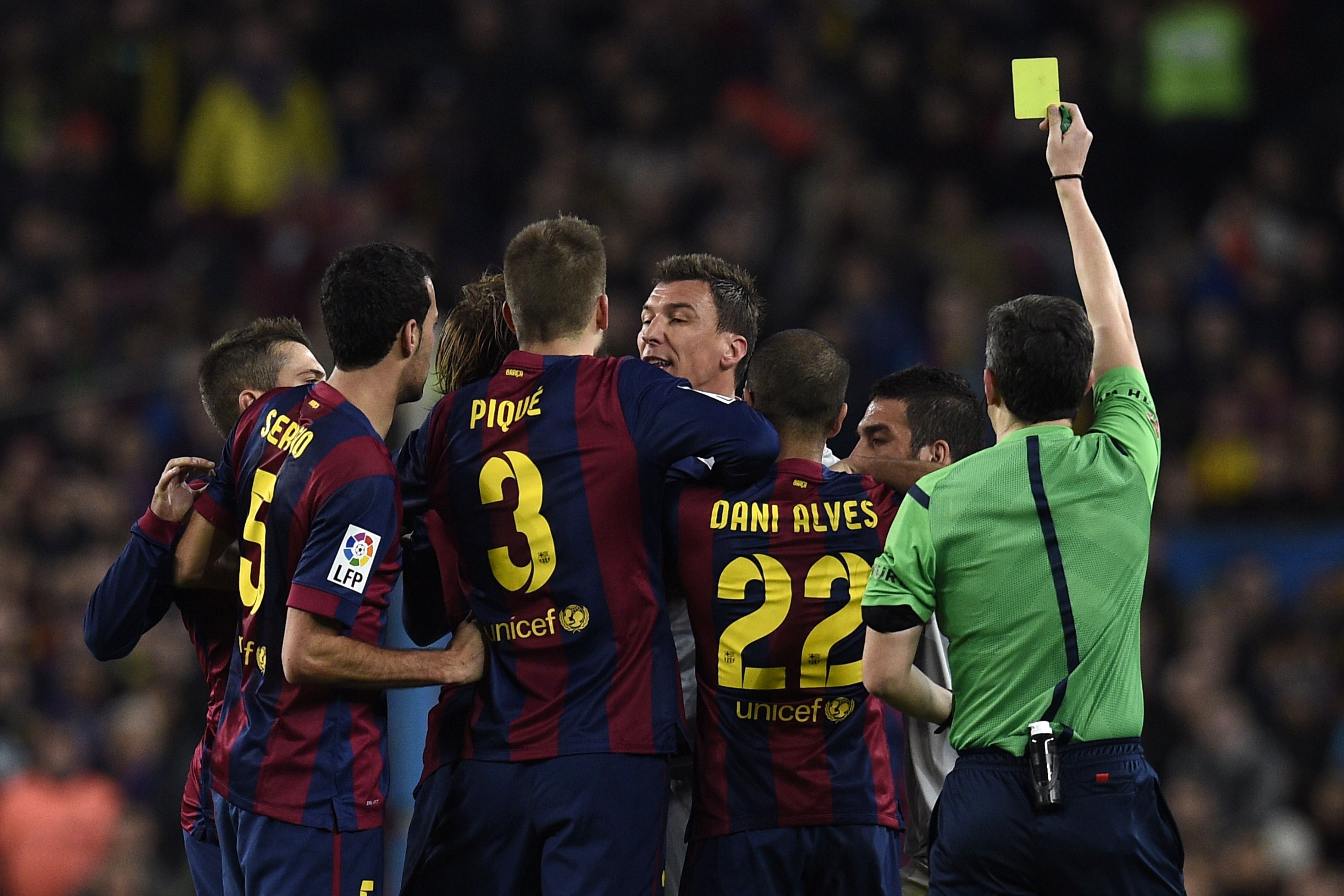 Players from Barcelona and Atletico argue as the referee hands out a yellow card. Photo: AFP