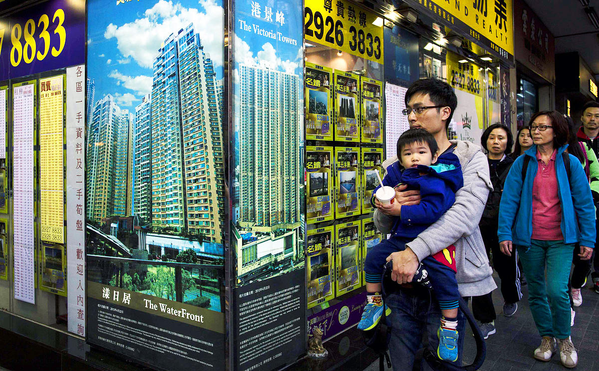 A man carrying a boy walk outside a property agency featuring posters of the latest high-rise apartment buildings. Photo: Reuters