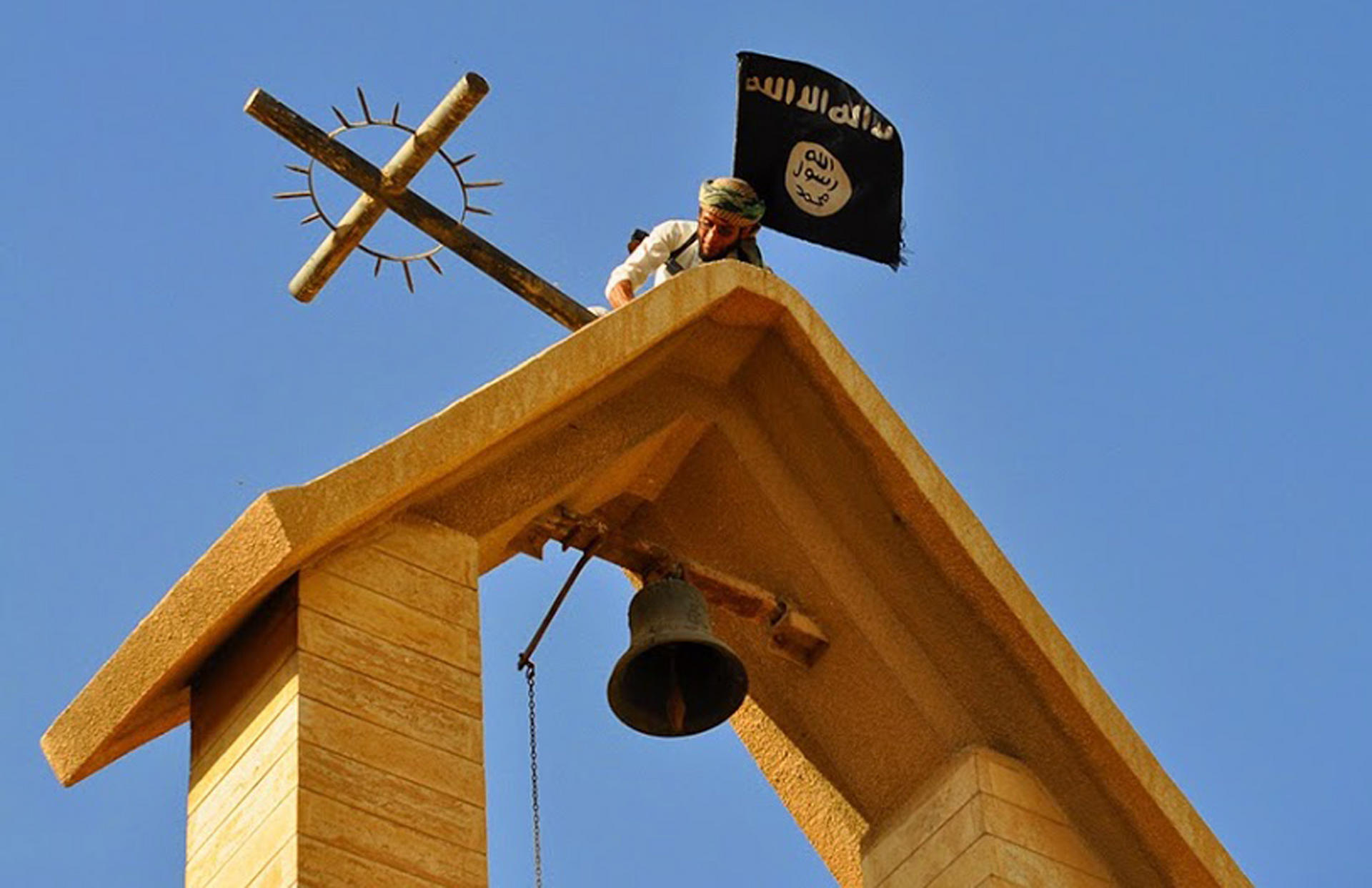 A member of Islamic State holds up its flag as he dismantles a cross on the top of a church in Mosul, Iraq, in this photo released by a militant website. Photo: AP