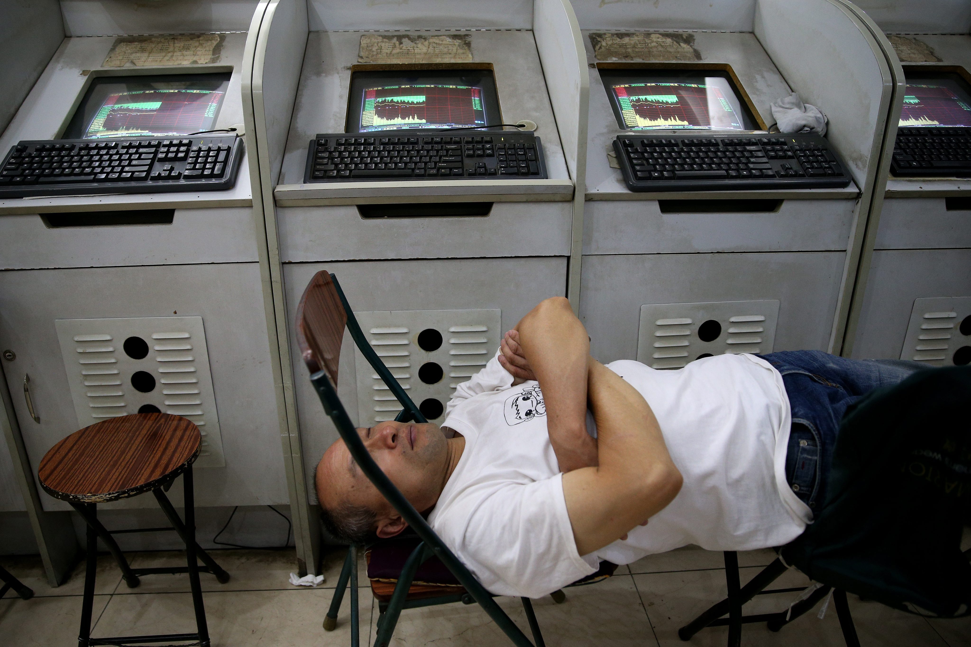 A stock investor takes a nap beside a line of computer screens showing stock prices at a brokerage house in Beijing city, China. Photo: EPA