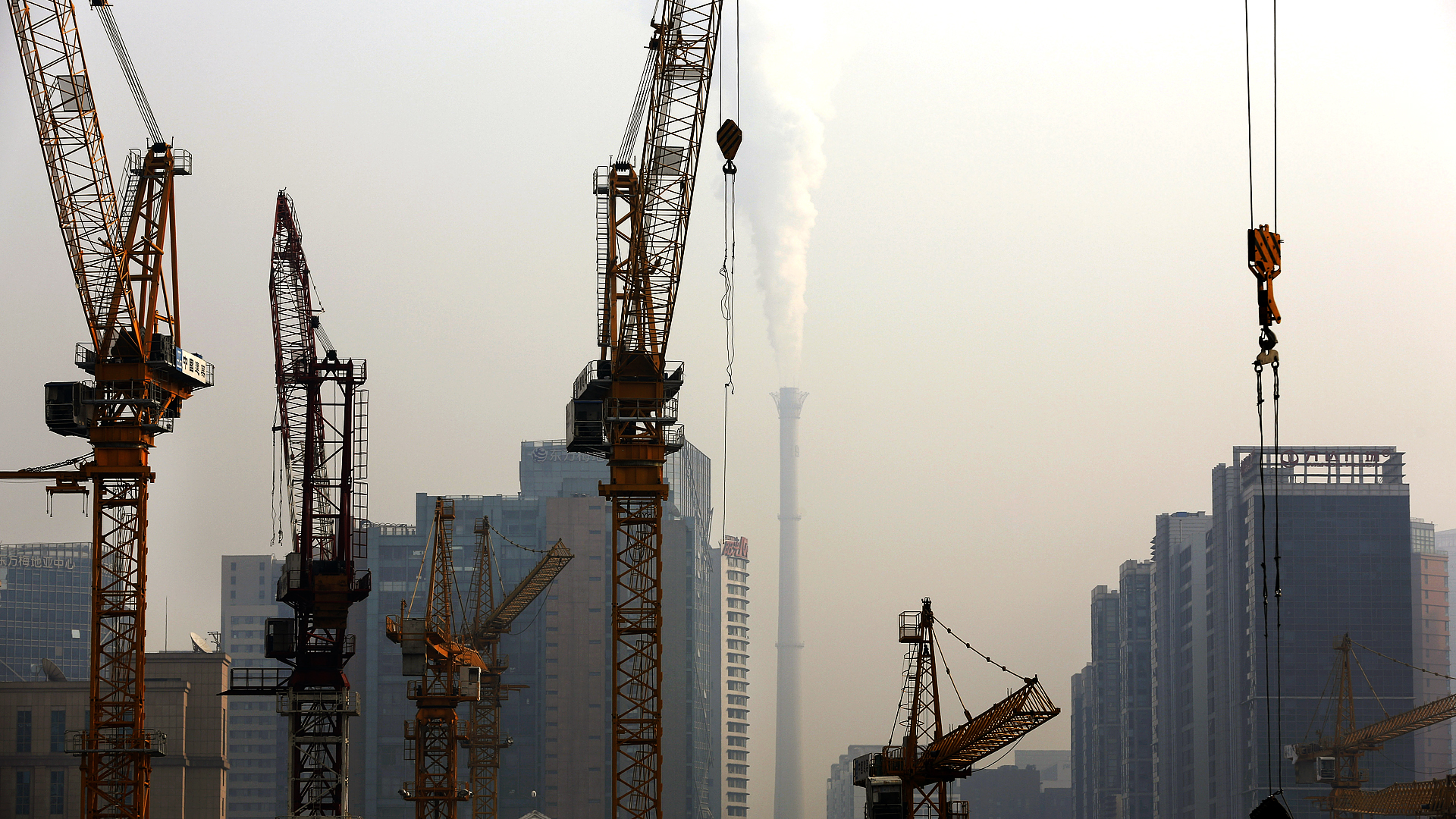 Cranes stand on a construction site as smoke belches from a coal-fired power station on a hazy day in Beijing. Photo: AP