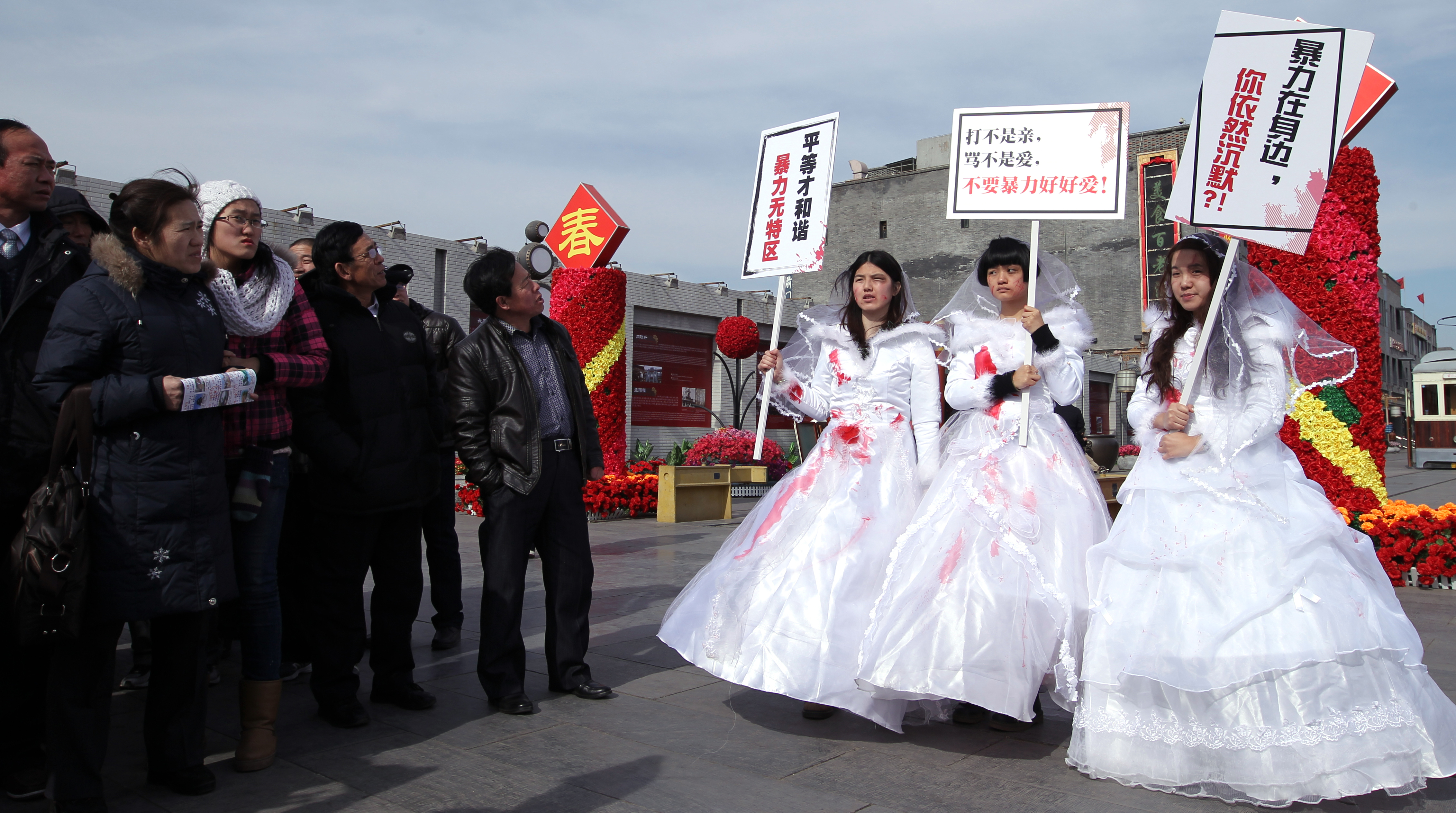 Three university student volunteers dress up with bloody wedding gowns in downtown Beijing to campaign for domestic violence victims as passersby look on. Photo: Simon Song 