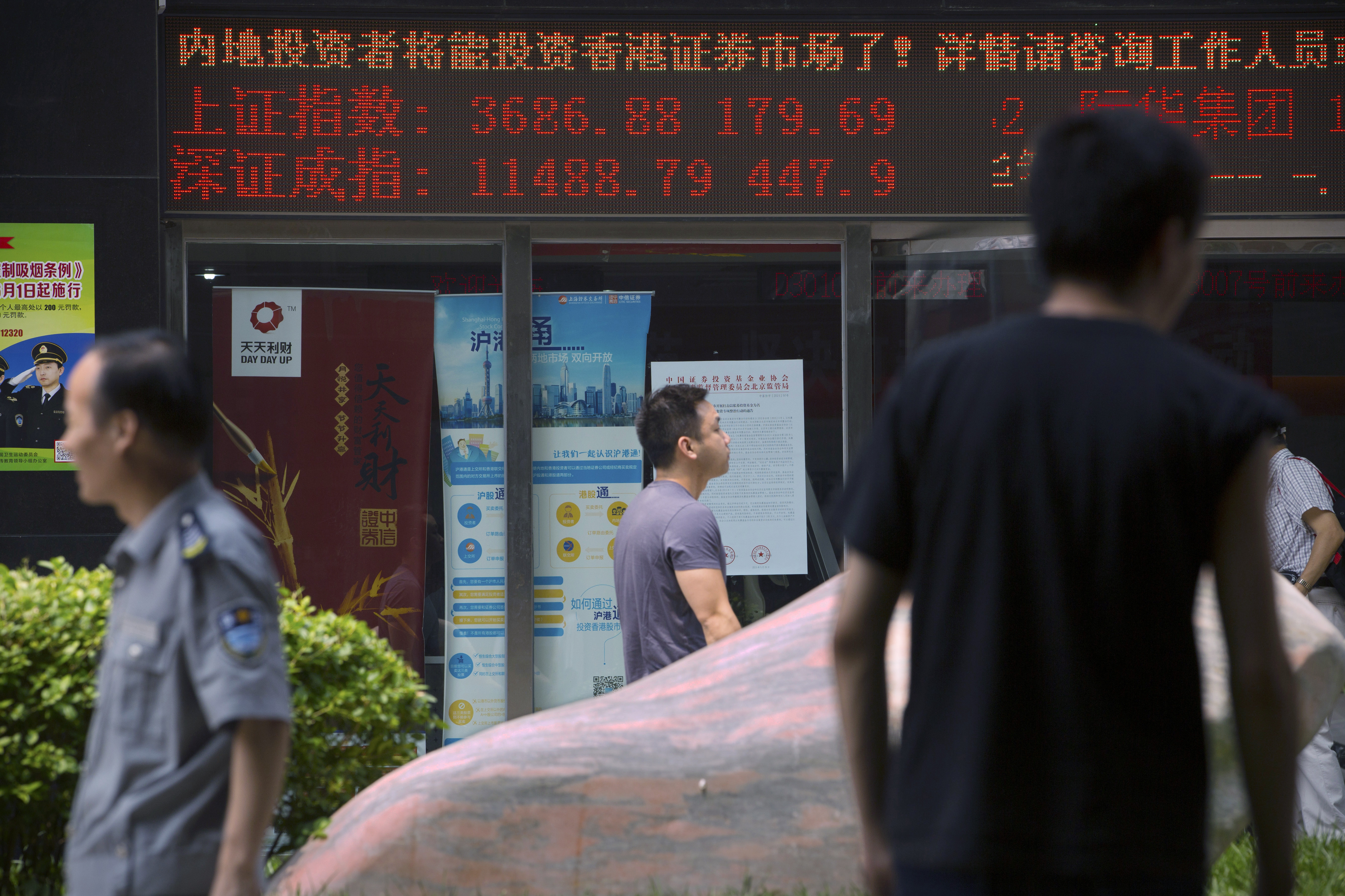 People walk outside of a stock brokerage displaying the values of the Shanghai, top, and Shenzhen stock indexes in Beijing. Photo: AP