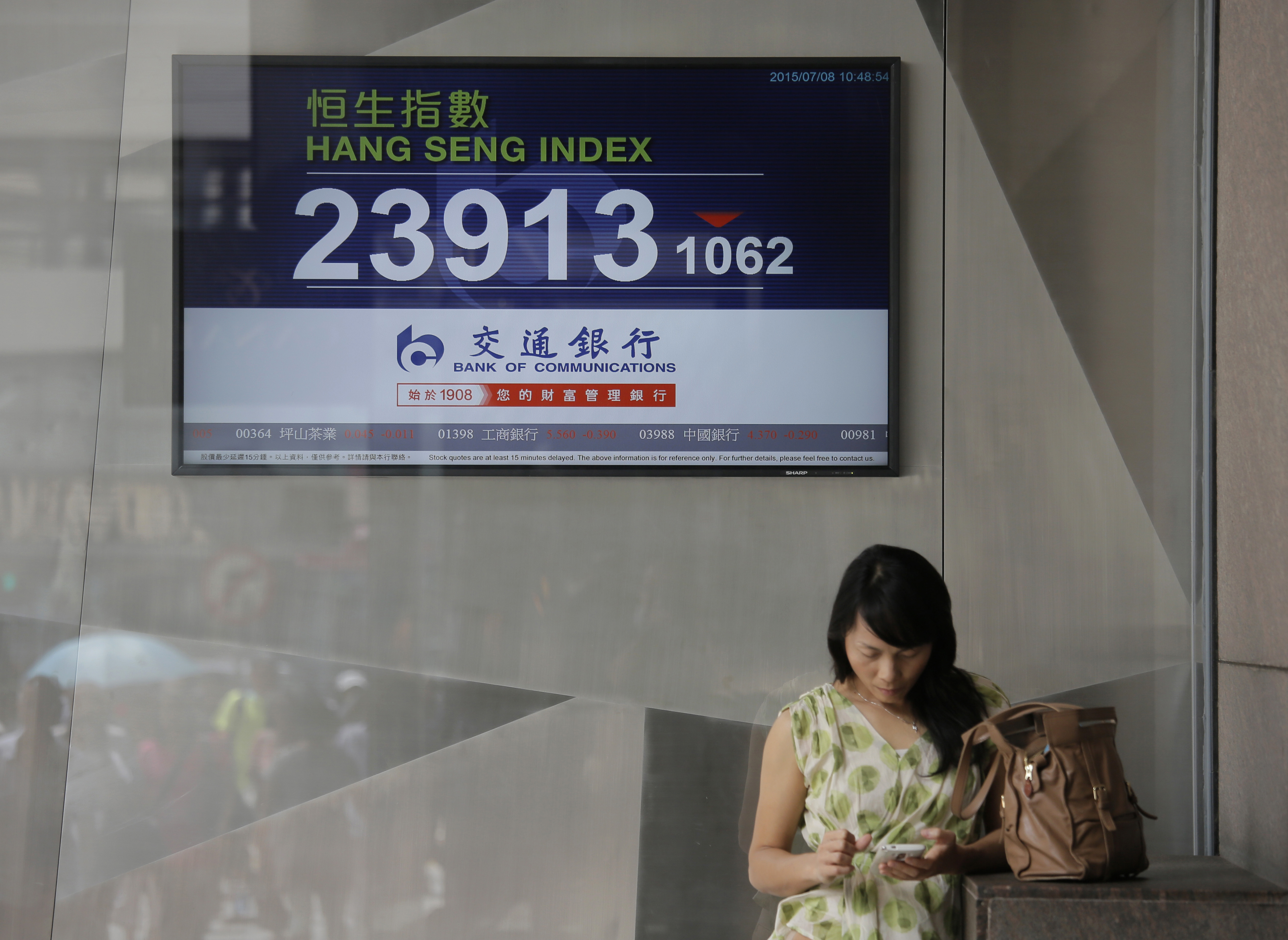 A woman stands in front of a screen showing the Hong Kong Hang Seng index near a local bank. Photo: AP