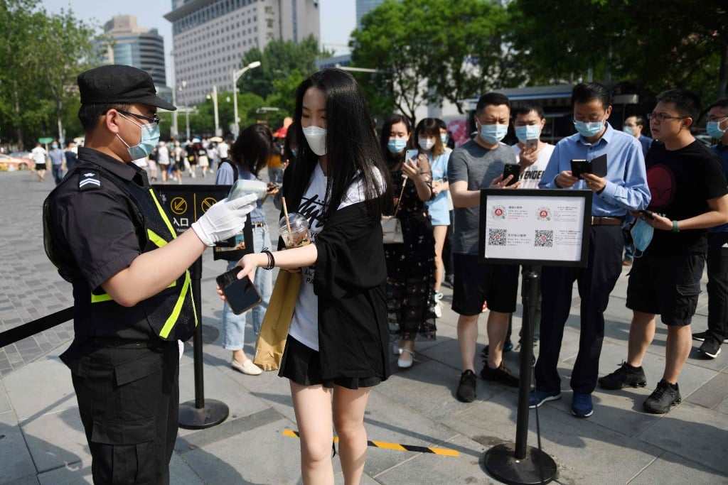 A woman has her temperature taken as others use smartphones to scan a code required to prove their health and travel status before being allowed to enter a shopping mall in Beijing on May 2. (Picture: AFP)