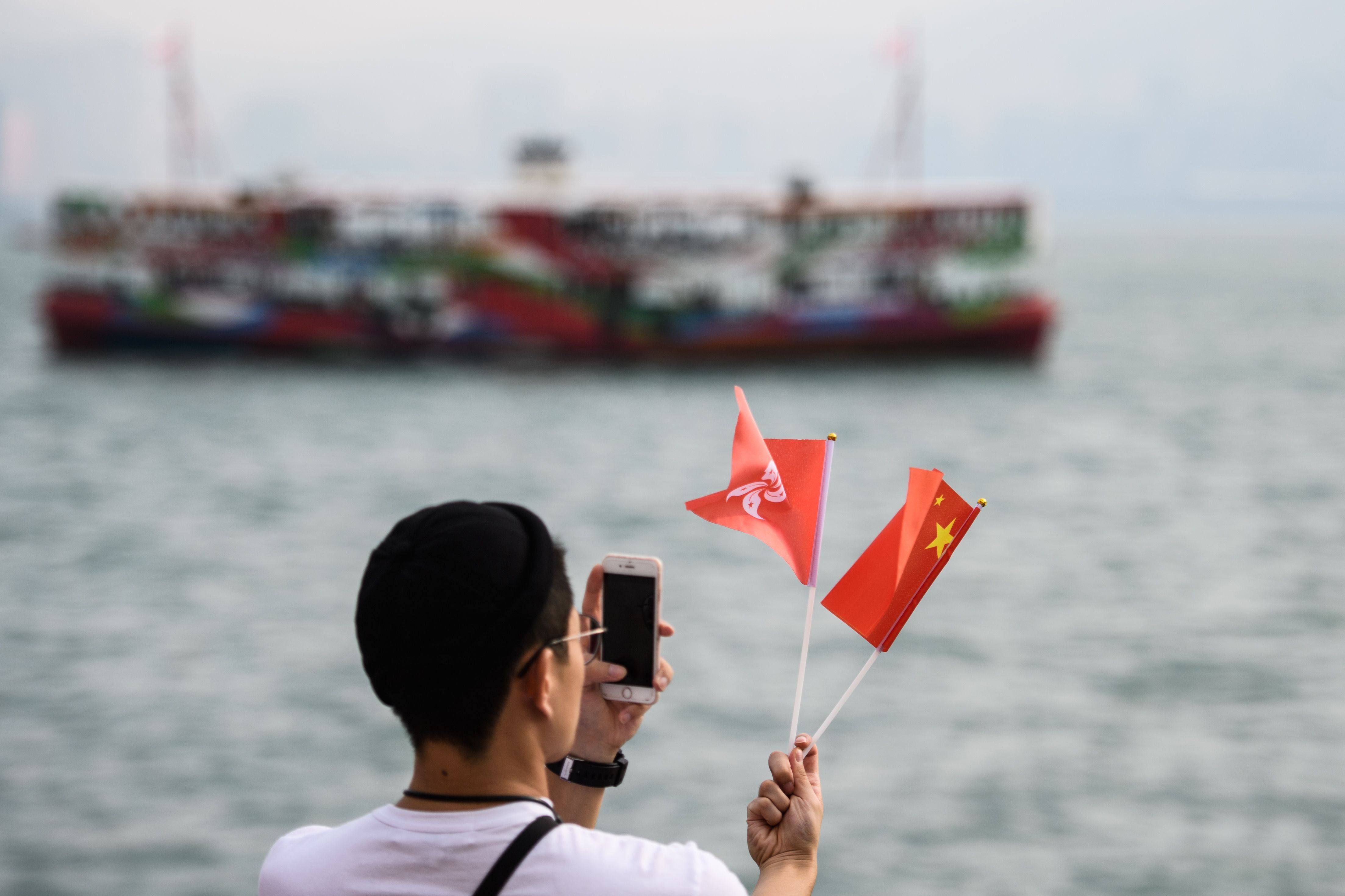 A man takes a photo of the Hong Kong and China flags as a Star Ferry sails past during National Day celebrations in Hong Kong on October 1, 2018. Photo: AFP