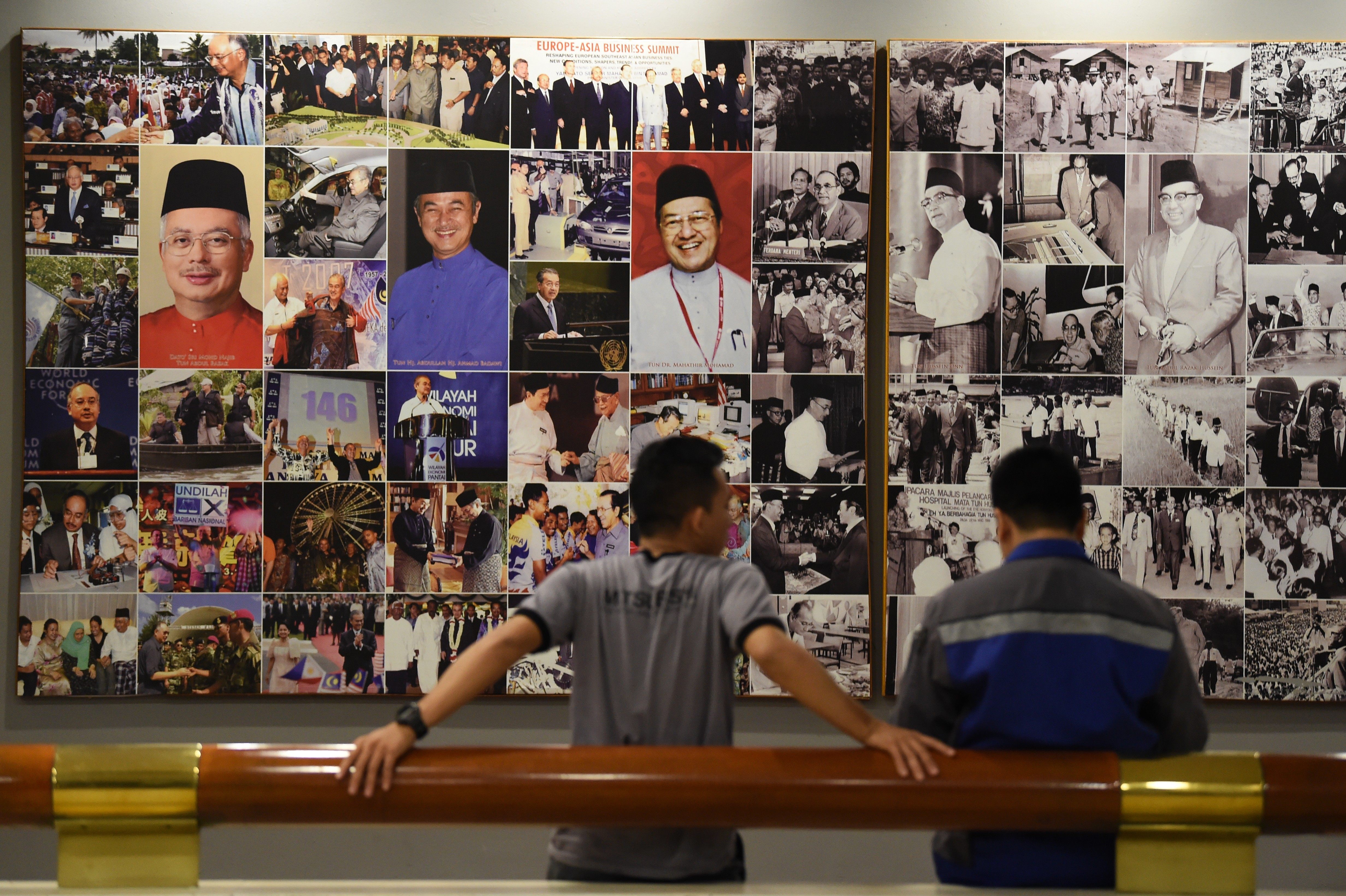 Two men stand in front of a wall of pictures of Malaysian leaders at the Umno headquarters in Kuala Lumpur. Photo: AFP