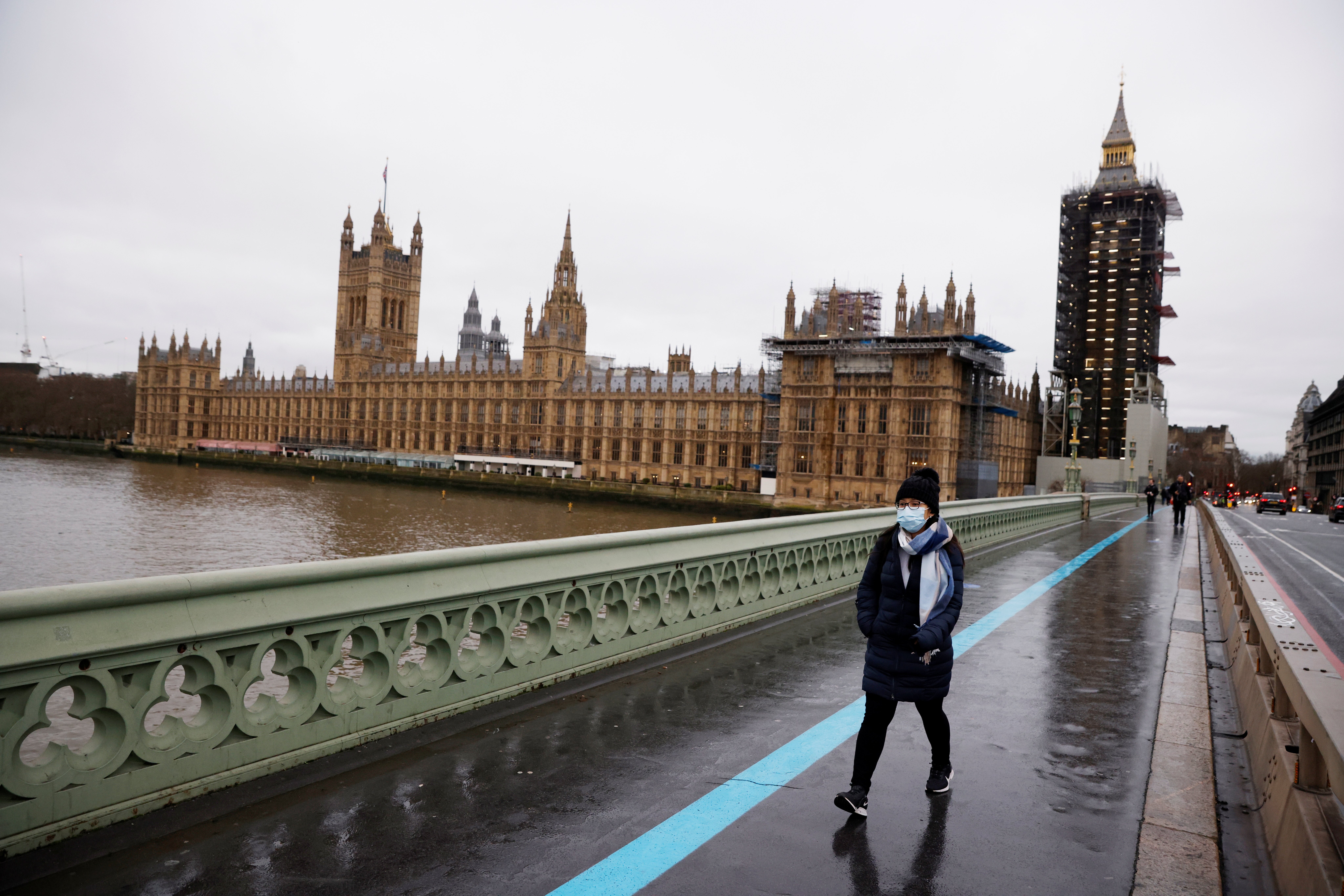 A woman wearing a face mask walks across Westminster Bridge past the Houses of Parliament, as the spread of the coronavirus disease (COVID-19) continues, in London, Britain, December 22, 2020. REUTERS/John Sibley