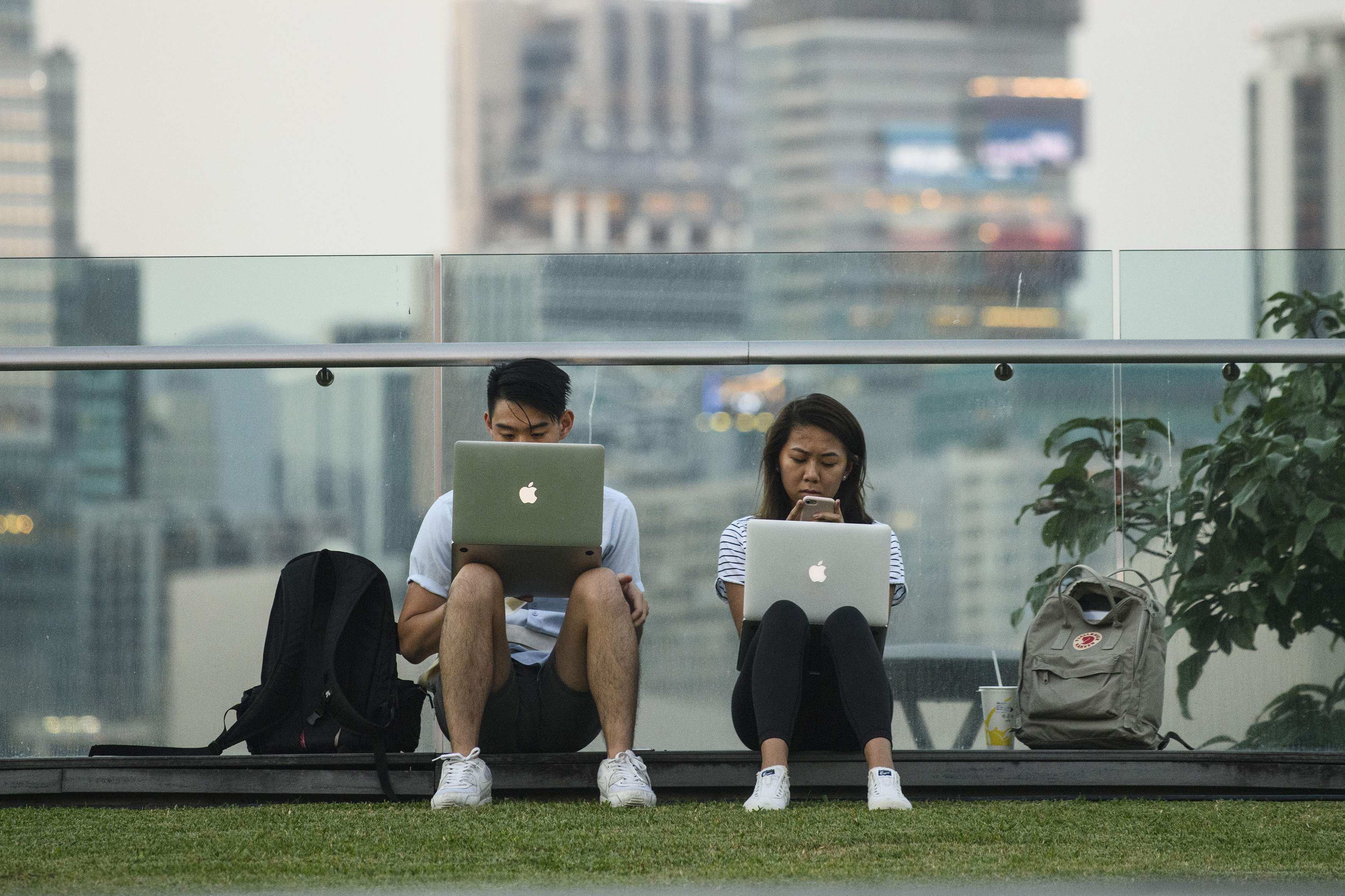 A man and woman use their laptops and a mobile phone as they sit in a park next to Victoria Harbour in Hong Kong in October 2017. Photo: AFP