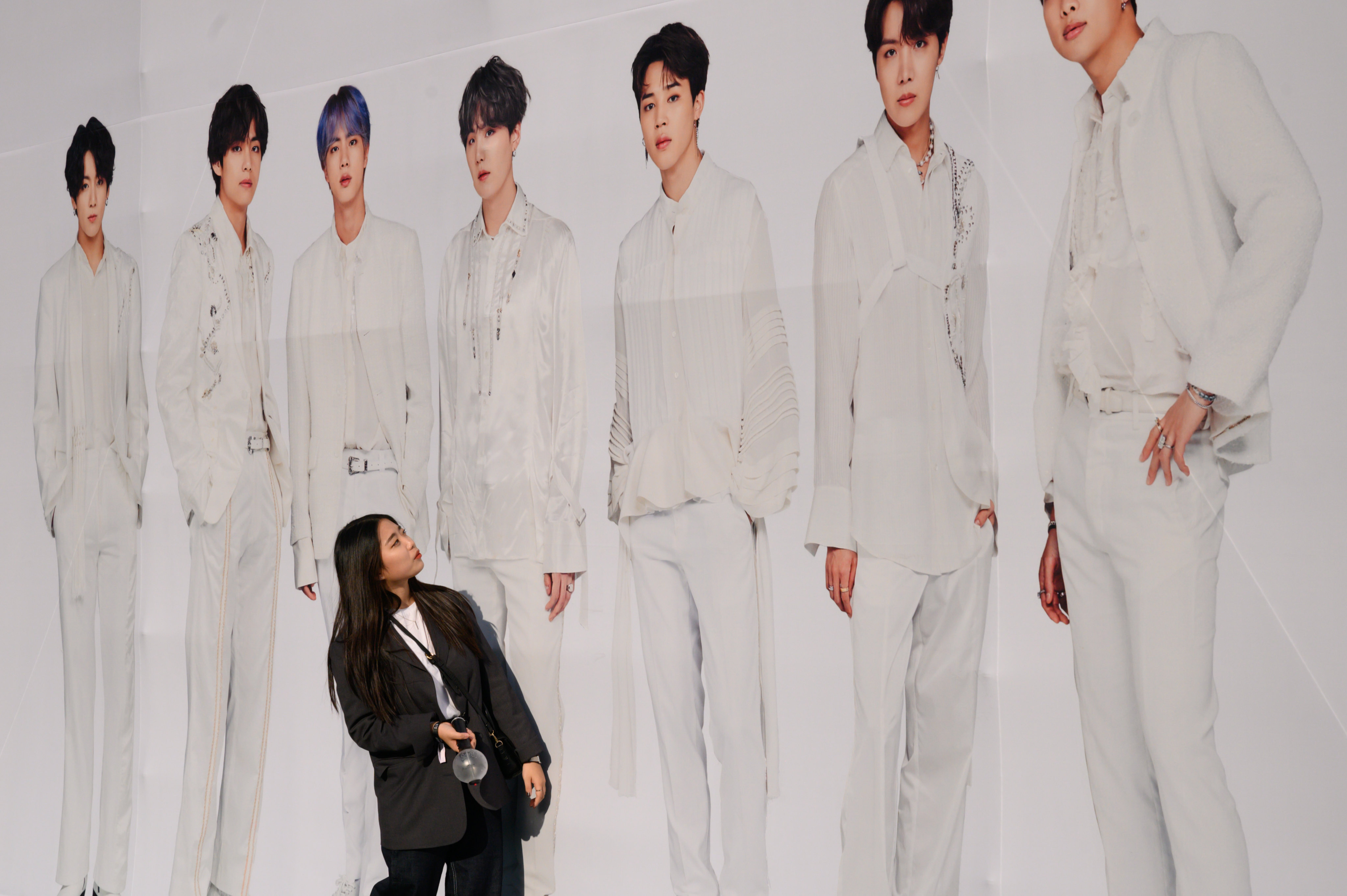 A fan of K-pop group BTS stands against a backdrop featuring an image of the band members as they arrive for the final concert of their world tour at the Olympic stadium in Seoul on October 29, 2019. The tour drew a total audience of more than 2 million at 62 shows in 23 cities, according to Big Hit Entertainment. Photo: AFP