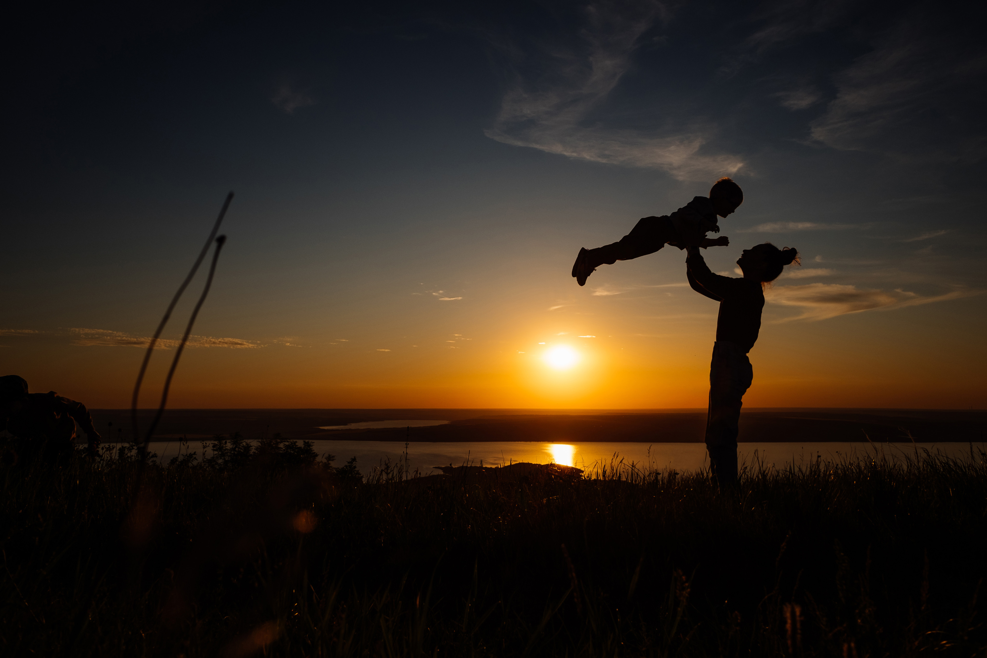 Silhouette of mother and baby raising baby in the air during beautiful sunset on lake background