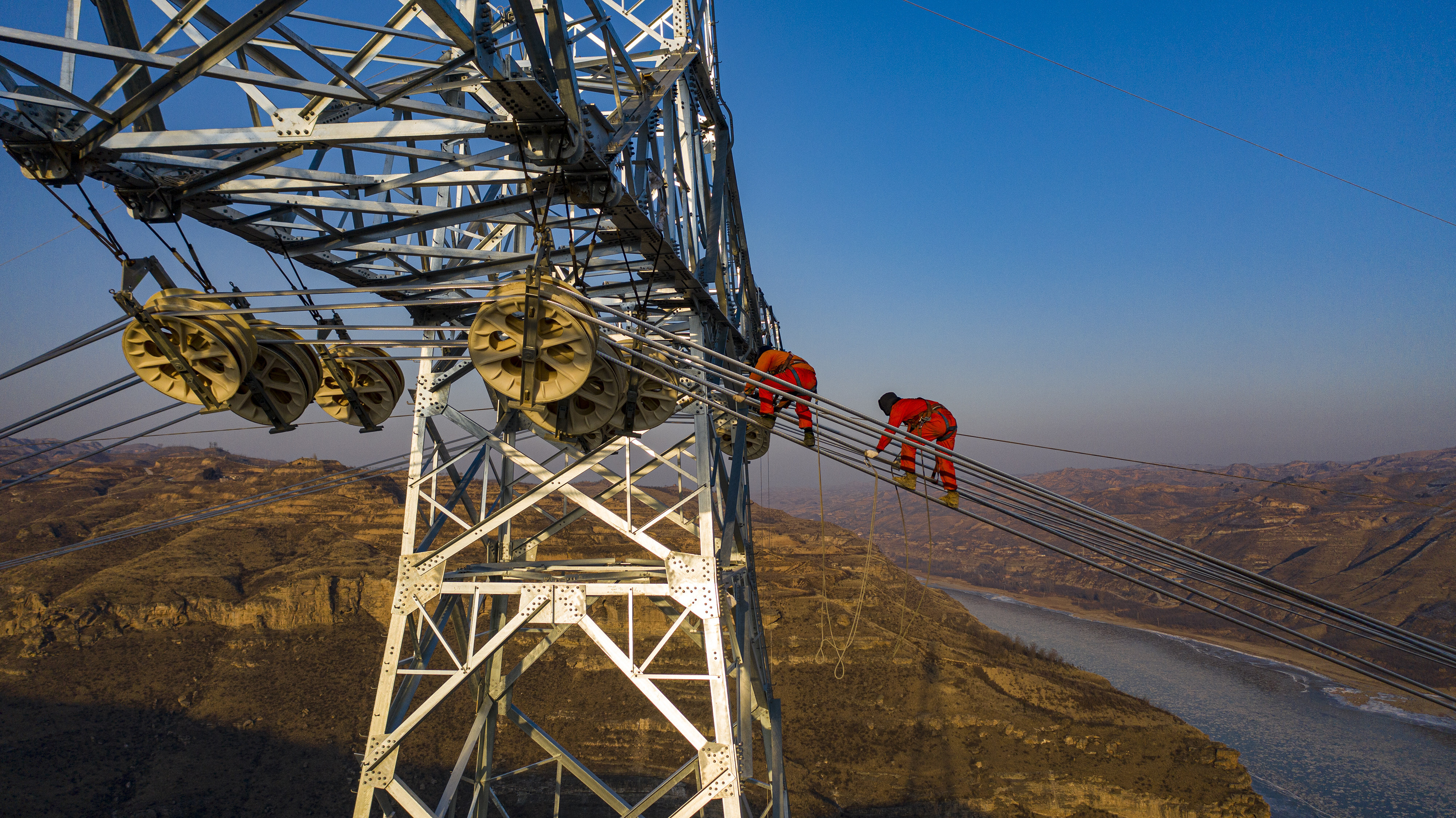 Electricians install electric wires on a transmission tower on the banks of China’s Yellow River during construction of an 800-kilovolt ultra-high voltage (UHV) power line on December 20, 2020 in Qingjian County, Shaanxi province, China. Photo: VCG via Getty Images