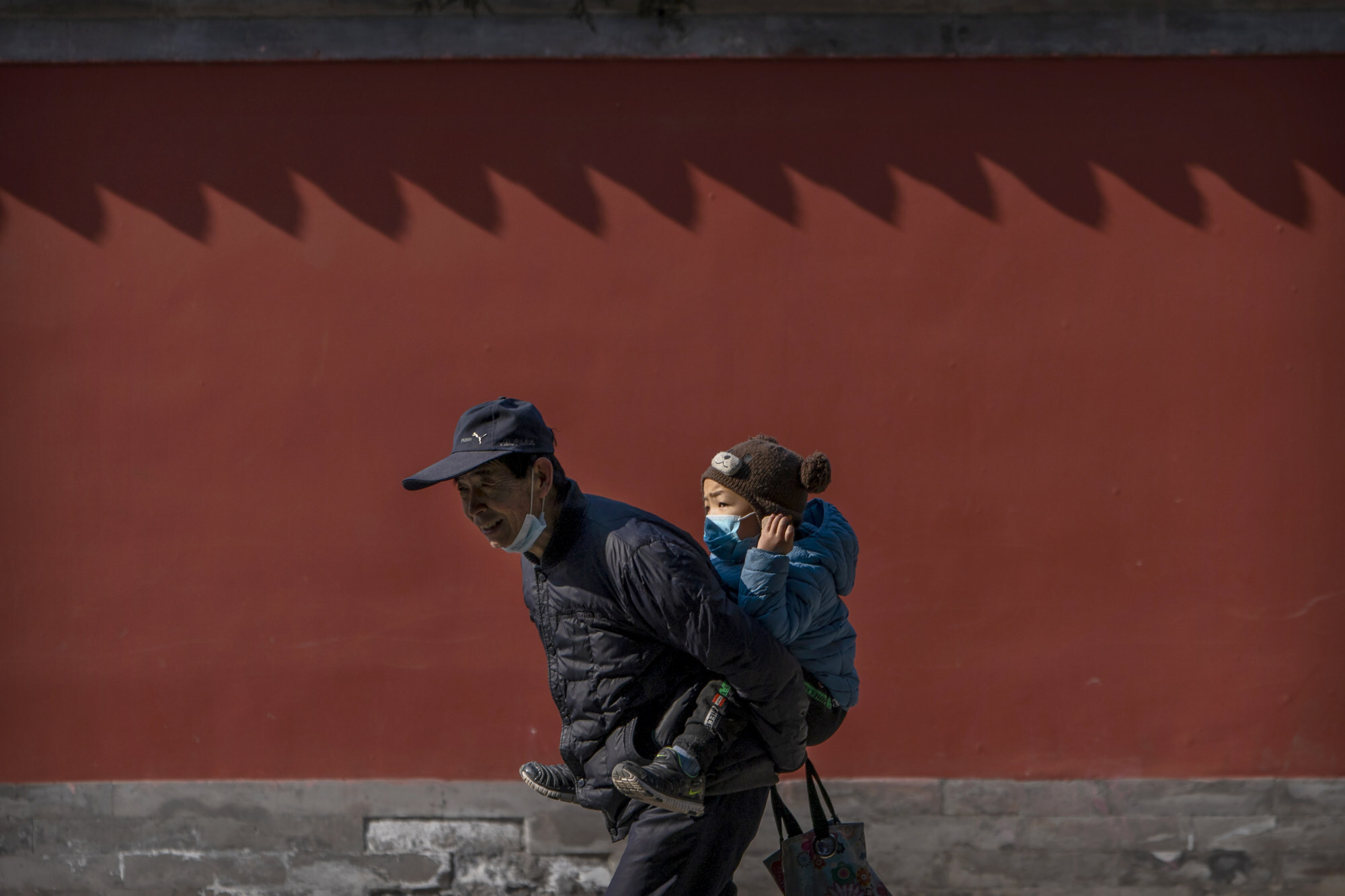 An elderly man carries a young boy as he walks through a public park in Beijing on February 9. Photo: AP